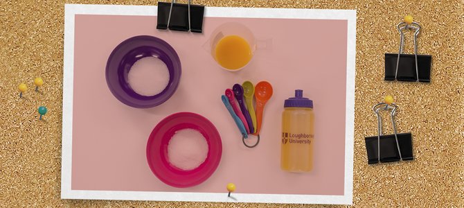 A Loughborough University branded water bottle, with some measuring spoons, juice and a bowl of sugar and salt next to it.